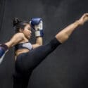 Young Asian woman boxer with blue boxing gloves kicking in the exercise gym, Martial arts on black background