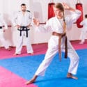 Tween girl mastering new taekwondo moves during group class with male coach